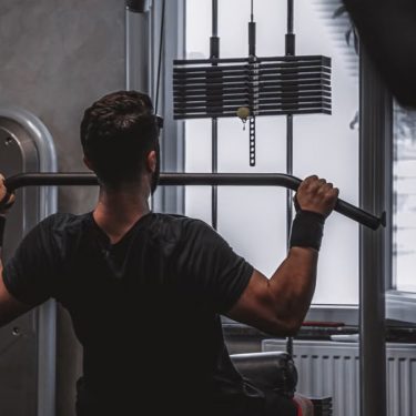 Back view of a man exercising with lat pulldown machine in the gym.