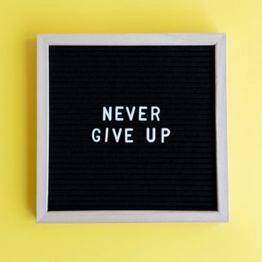 Black felt board with 'Never Give Up' on a bright yellow background for motivation.
